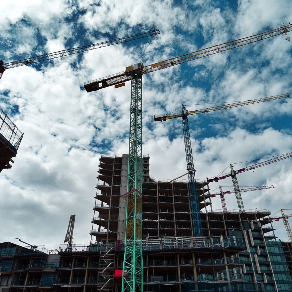 Construction cranes over building site against cloudy sky.